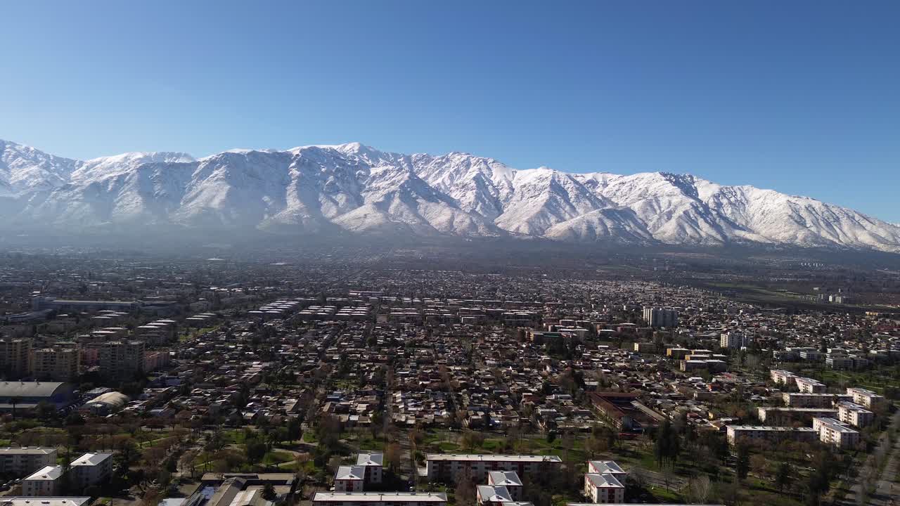 Zoom di un drone sulle Ande innevate dal distretto di Nunoa a Santiago, che mostra i tetti urbani in contrasto con le cime innevate sotto la luce del giorno