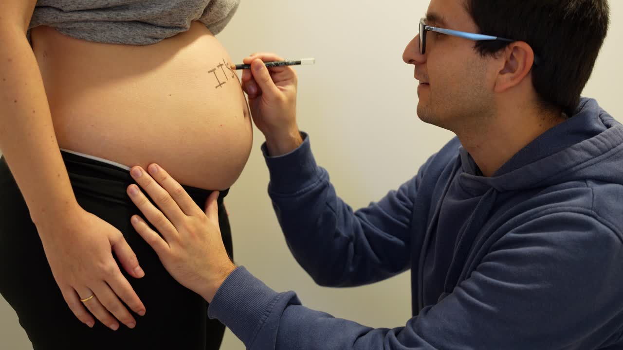 Happy man revealing the baby gender by painting on the belly of his wife