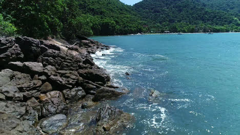 bajo vuelo aéreo sobre las olas del mar chocando contra las rocas en un día soleado, brasil