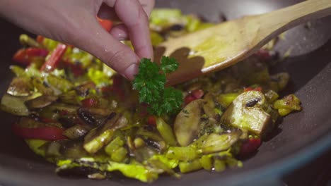 a cook puts parsley as decoration on the ingredients cooking in a frying pan