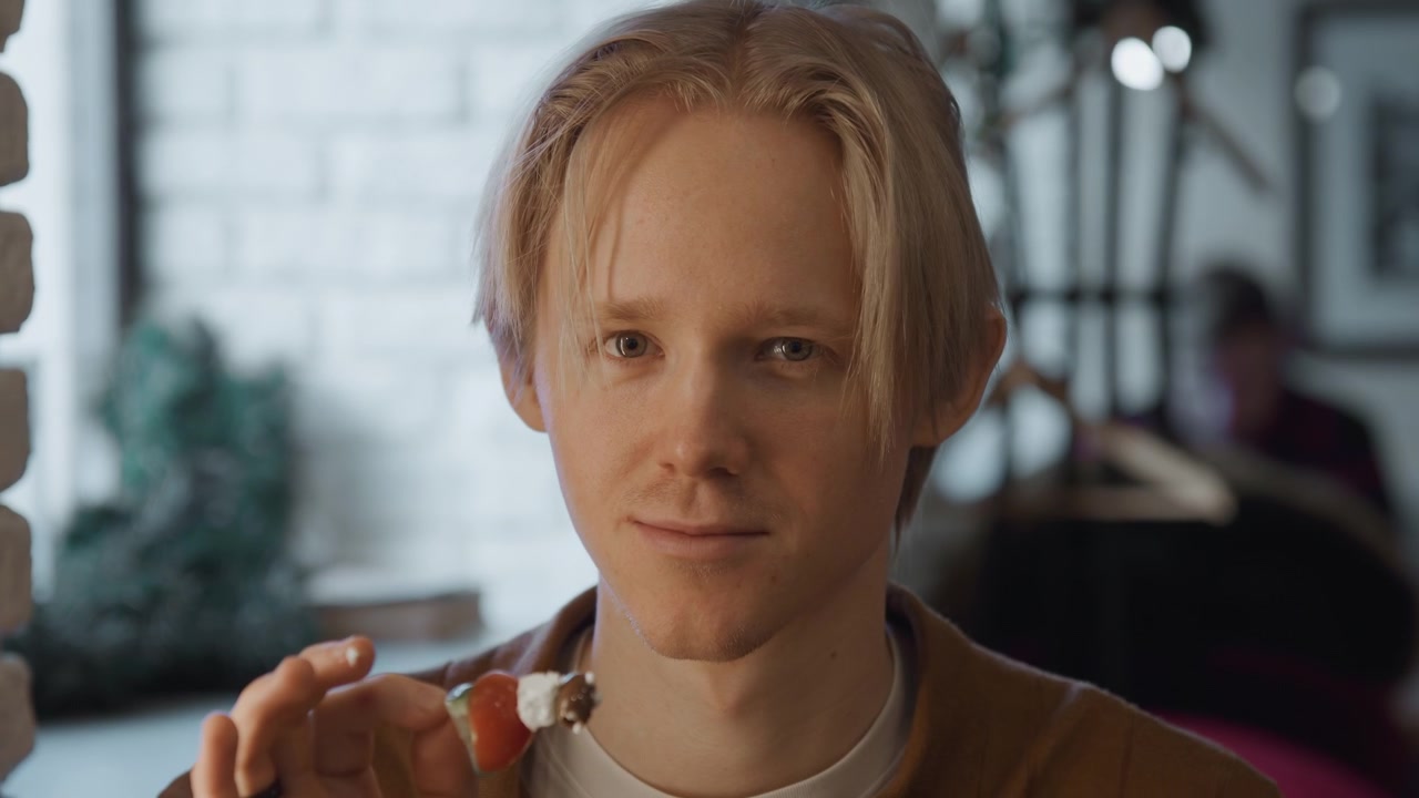 Close up of young man holding and eating food indoors with soft lighting. subject wears casual clothing interacting naturally in everyday setting with visible background elements like brick