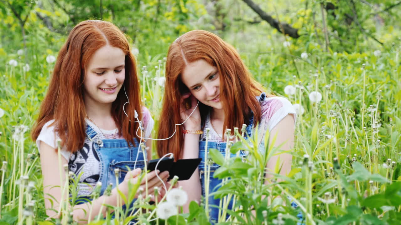 두 명의 빨간 머리 쌍둥이 자매가 헤드폰 1에서 음악을 듣습니다.