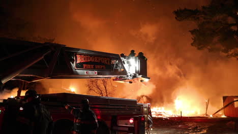 a group of firemen load up into the ladder platform as a huge orange plume of smoke looms in the background