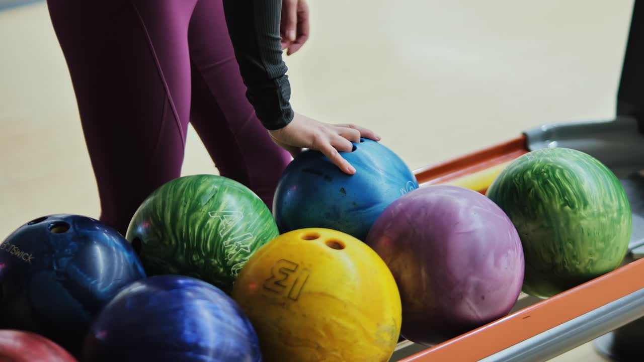 Close-up of woman's hand selecting blue bowling ball in colorful indoor setting