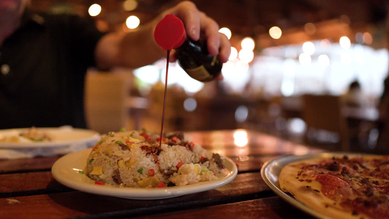A person pours dark soy sauce over a plate of fried rice at dinner