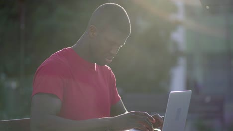 young afro-american muscular man typing on laptop in park
