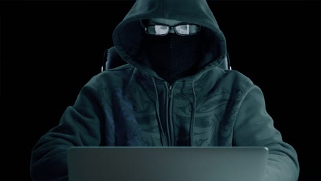 hombre con capucha sentado en la mesa y codificando en el portátil. vista frontal de cerca. hacker con máscara de balaclava y gafas trabajando en la computadora. navegando por internet hombre con fondo de hormigón. clave de croma del canal alfa.