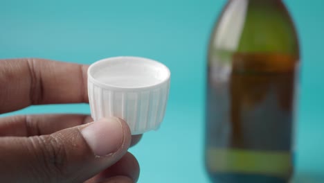 primer plano de un frasco de medicamento con una tapa llena de líquido