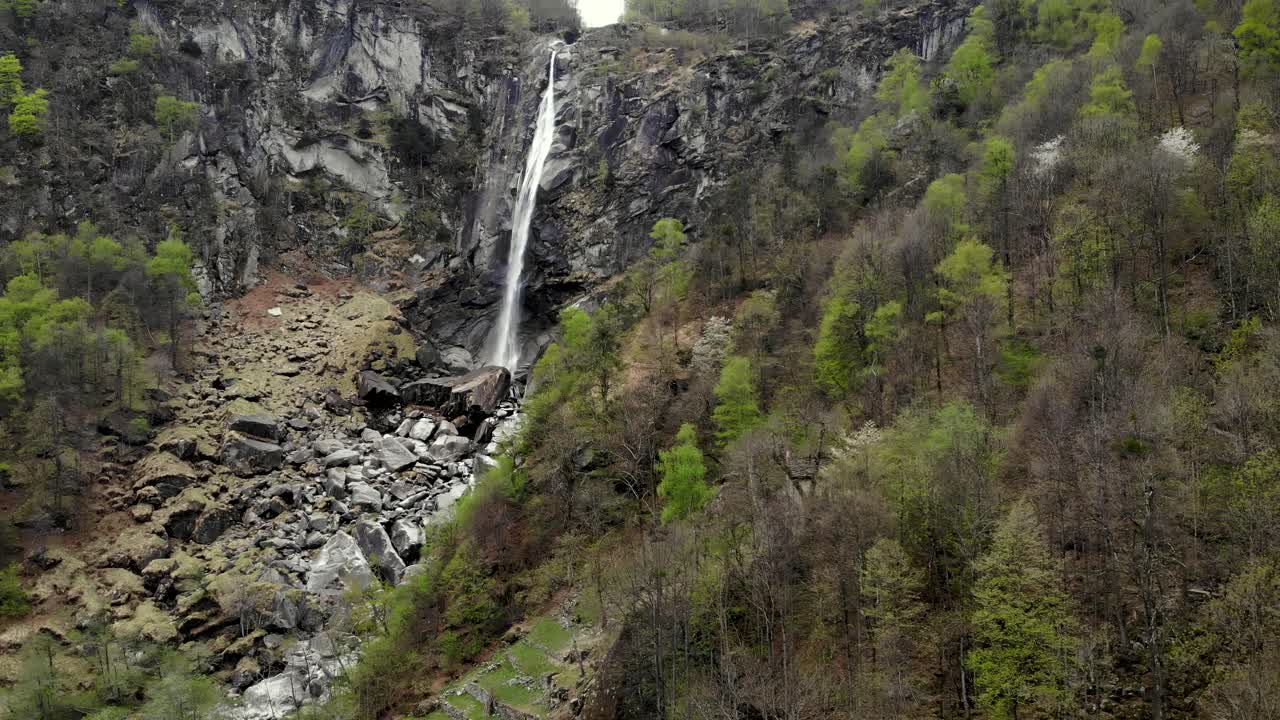 sobrevuelo aéreo sobre el paisaje alpino primaveral de foroglio en ticino, suiza con un movimiento de cámara panorámica desde la cascada hasta los tejados de las antiguas casas de piedra en el pueblo