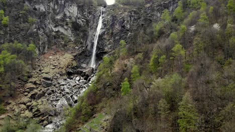 aerial flyover over the spring alpine landscape of foroglio in ticino, switzerland with a pan down camera motion from the waterfall down to the rooftops of old stone houses in the village