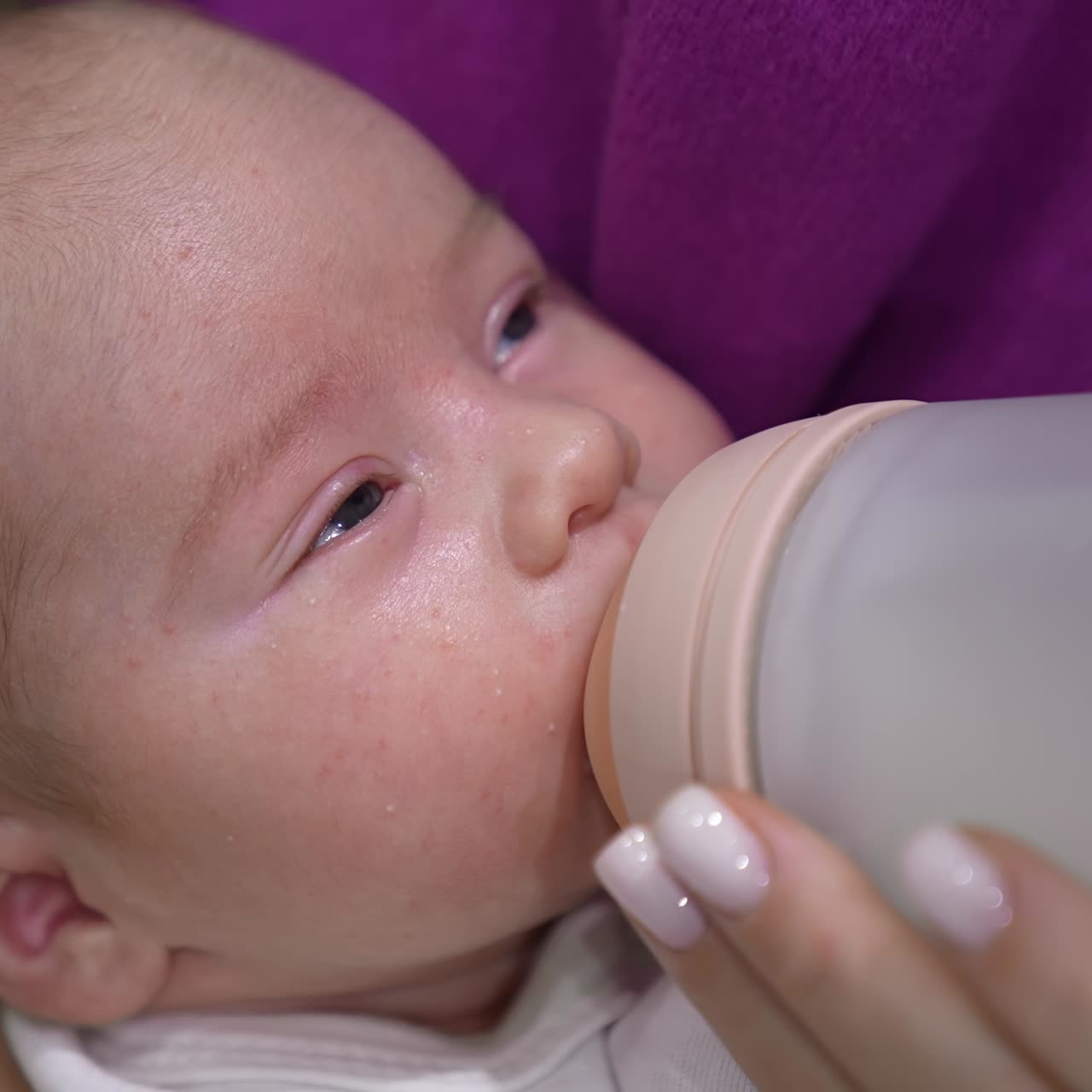 Beautiful sleepy baby suckling milk from a bottle. Mother's feeding her child holding him in hands. Close up