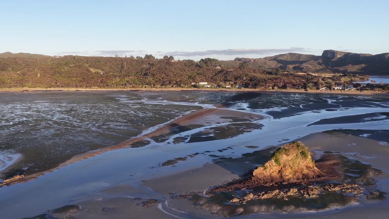 Drone som trekker seg tilbake over tidevannsestuar og ulendt kystlinje på Sørøya, New Zealand, med fantastisk natur og miljø.