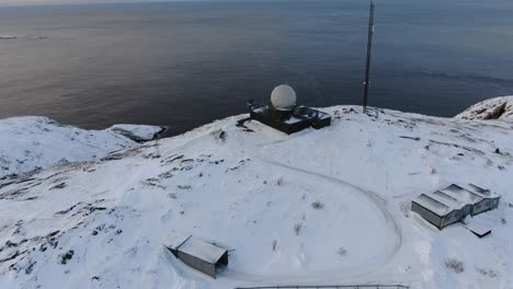 drone view in tromso area in winter flying over a snowy mountain peak and into the ocean in norway vertical lift