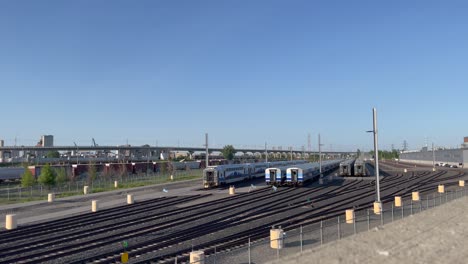 VIA-Rail-Siemens-Venture-Train-Running-Behind-Several-Parked-EXO-Trains-in-a-Railyard-in-Montreal,-Quebec