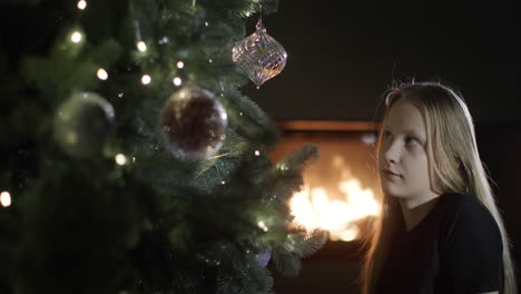 la niña está mirando un hermoso árbol de navidad, al fondo arde un fuego en la chimenea. nochebuena