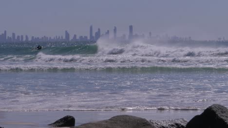 ocean waves and surfers with gold coast skyline in foggy background. rainbow bay, qld, australia, wide shot
