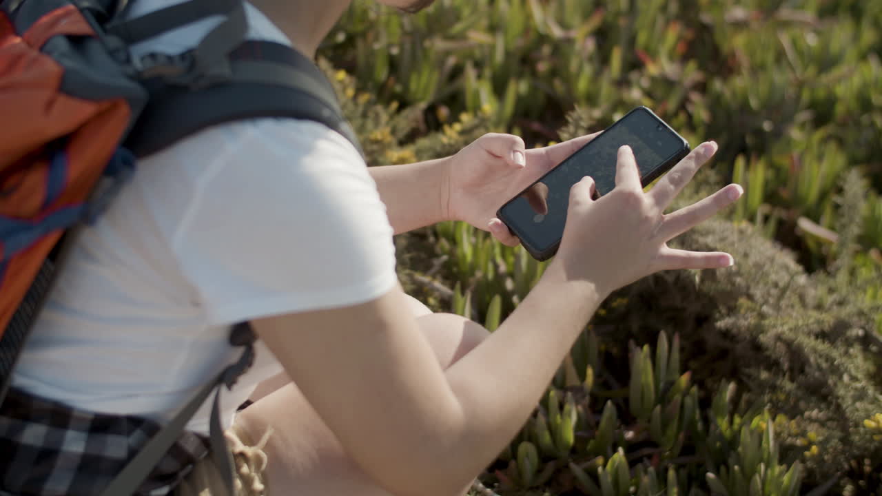 Close up of Caucasian girl with backpack making photo of flowers with phone