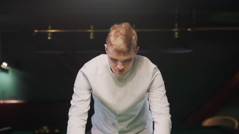 close-up of focused young man in white shirt holding triangle rack in billiard room under warm ambient lighting, concentrating on arranging pool balls with precision, surrounded by modern decor