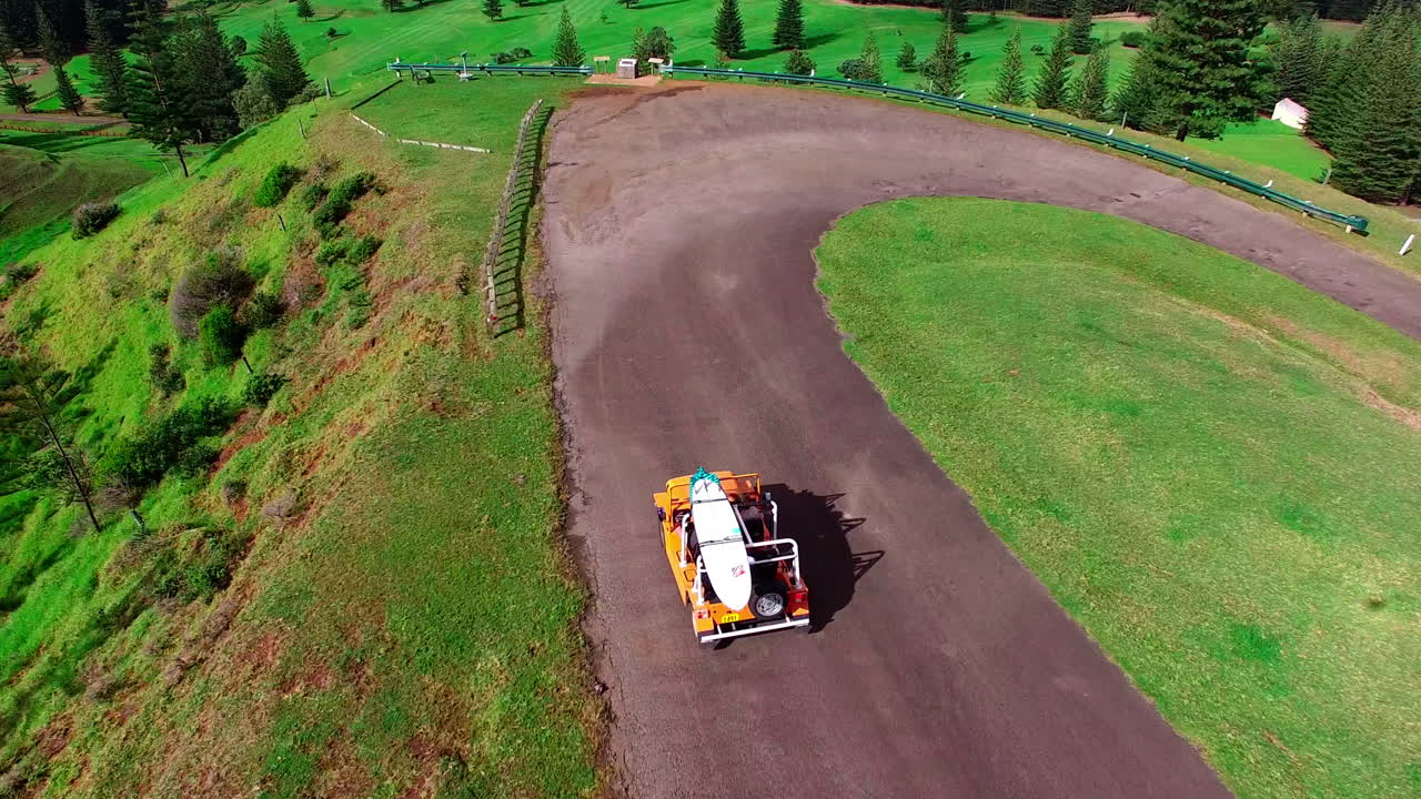 서프보드 를 고 있는 밝은 노란색 지프 가 노르폴크 섬 의 도로 를 탐험 하고 있다