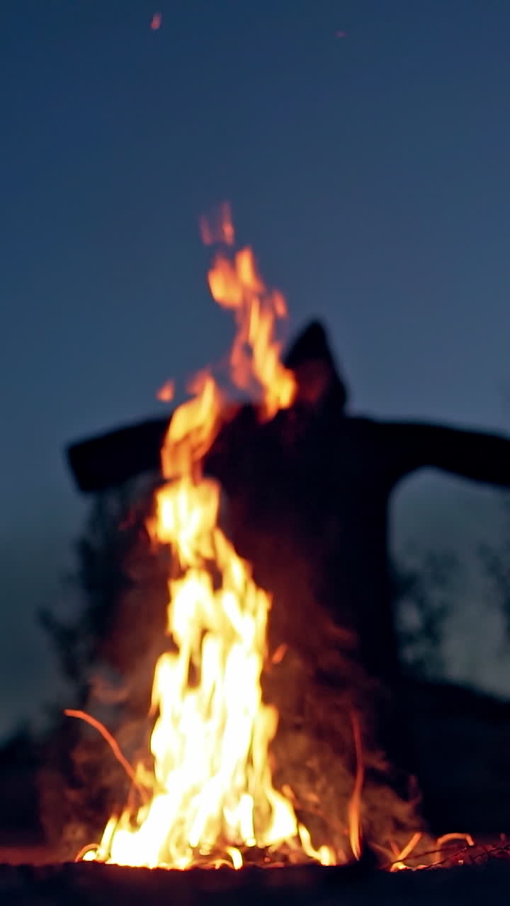 Horrible atmosphere at night outside. Bright flame with orange sparkles and dark nightmare with outstretched arms. Fright concept. Vertical video