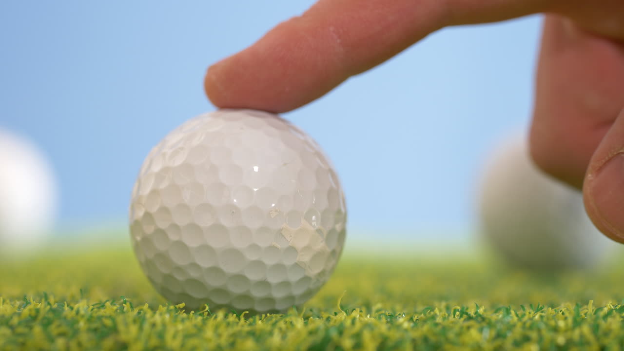 실내 골프 코스에서 인공 잔디 위에 손가락으로 굴러가는  골프 공의 느린 동작  - 근접