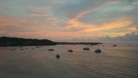 Magnífica-Vista-Aérea-Vuelo-Volar-Hacia-Atrás-Imágenes-De-Drones-En-La-Hora-Dorada-Puesta-De-Sol-De-Ensueño-Con-Nubes-Coloridas-Reflejadas-En-La-Bahía-De-Hongos-Lembongan