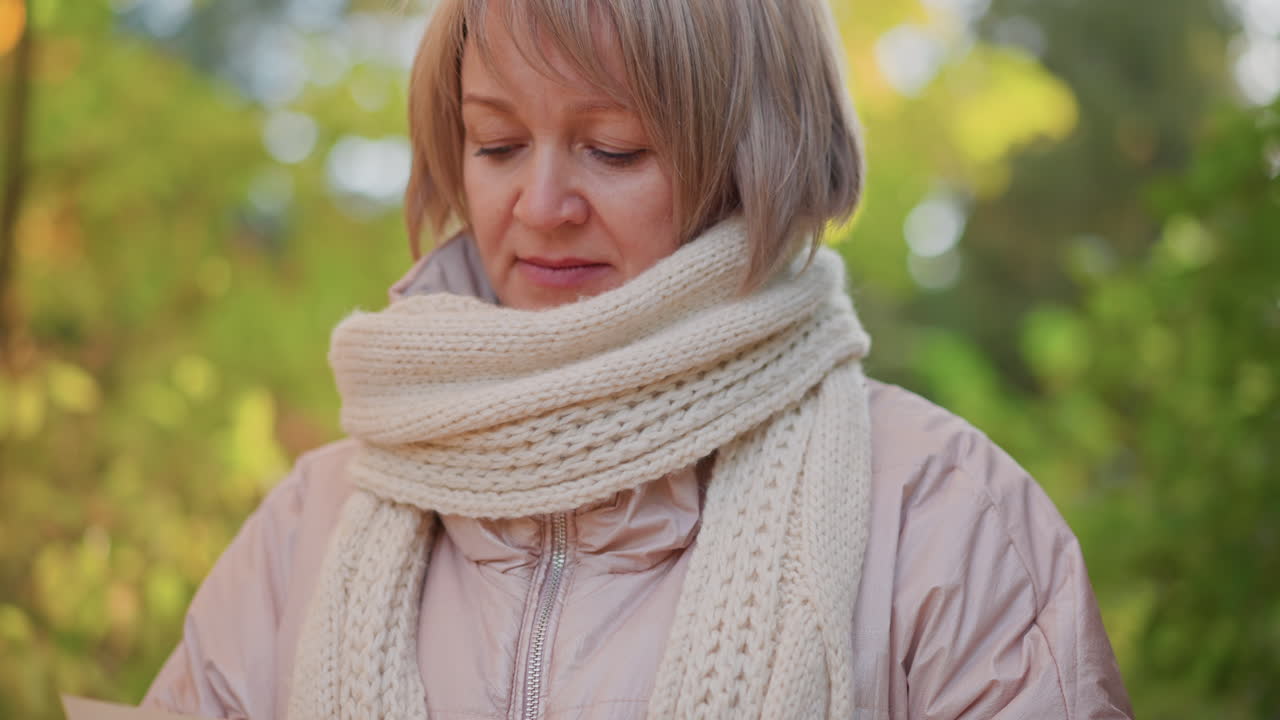 close up of woman reading book while walking through autumn forest, flipping page with crimson leaf on fingers, knitted scarf framing face, tranquil moment capturing contemplative seasonal journey