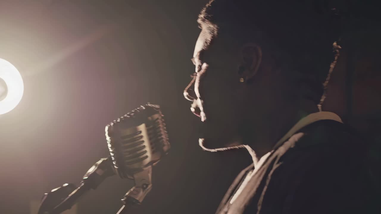 Moody video scene of a singer in profile, captured in low light with a vintage microphone