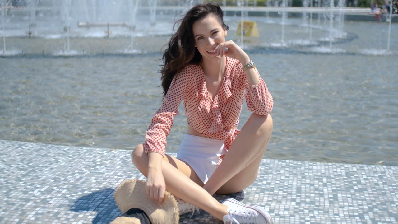 портрет красивой девушки в красочной летней одежде, сидящей у фонтана
