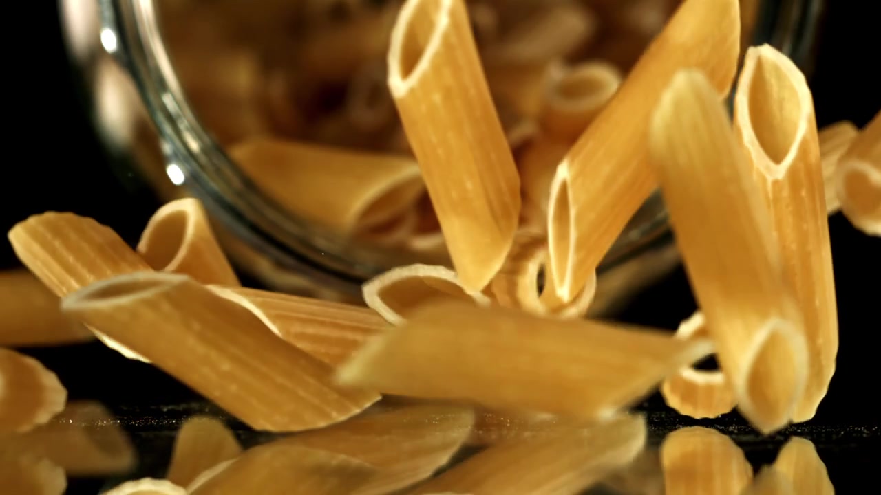 Penne che cadono al rallentatore su una superficie nera riflettente