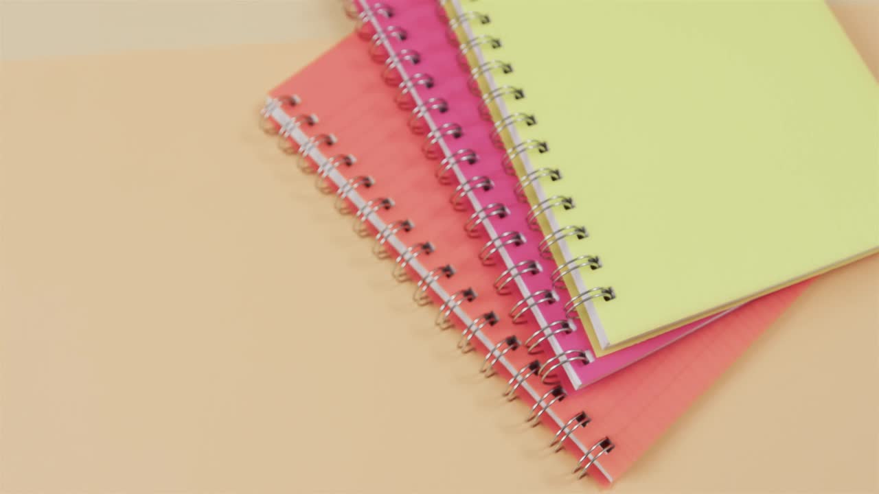 Overhead view of colourful notebooks on beige background, in slow motion