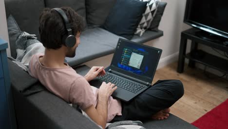 caucasian man in headphones scrolling social media on laptop at home