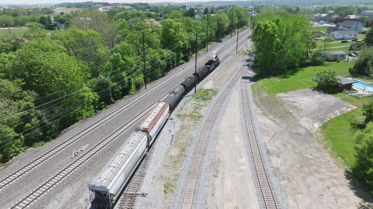 A vintage steam freight train makes its way backing up in yard performing switching operations moving steadily along the railway tracks in a peaceful countryside setting