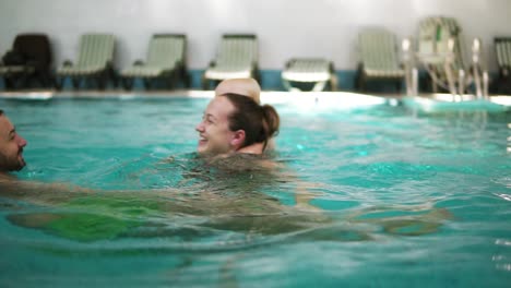 Young-family-swimming-in-the-pool-together-with-his-cute-little-child.-The-boy-is-swimming-on-the-back-of-his-mother.-Happy-family-having-fun-in-the-pool