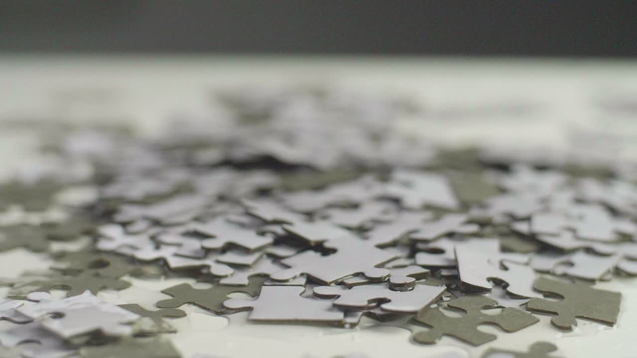 Water drops falling on a white and gray puzzle pieces laying randomly on a white surface. Shot in 4K;  Shallow depth of field.