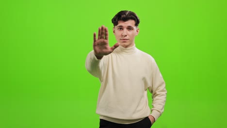 the man is standing and looking at the camera. he is raising his hand and says stop. he is standing on a green background. green screen. 4k.