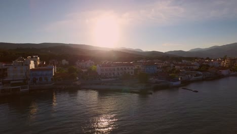 Aerial:-Small-fishing-town-with-Greek-flag-on-Samos-island,-Greece