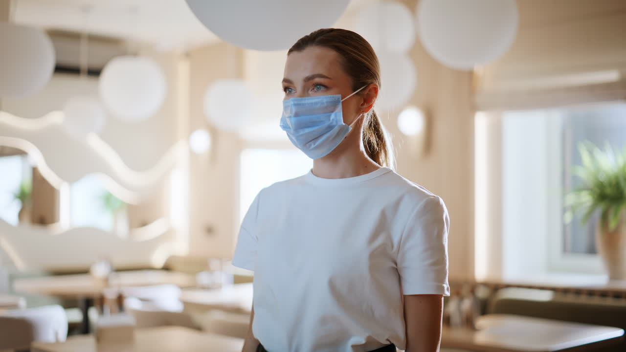 Servitør som bruker medisinsk maske i en restaurant. Kvinne tar vare på helsen.