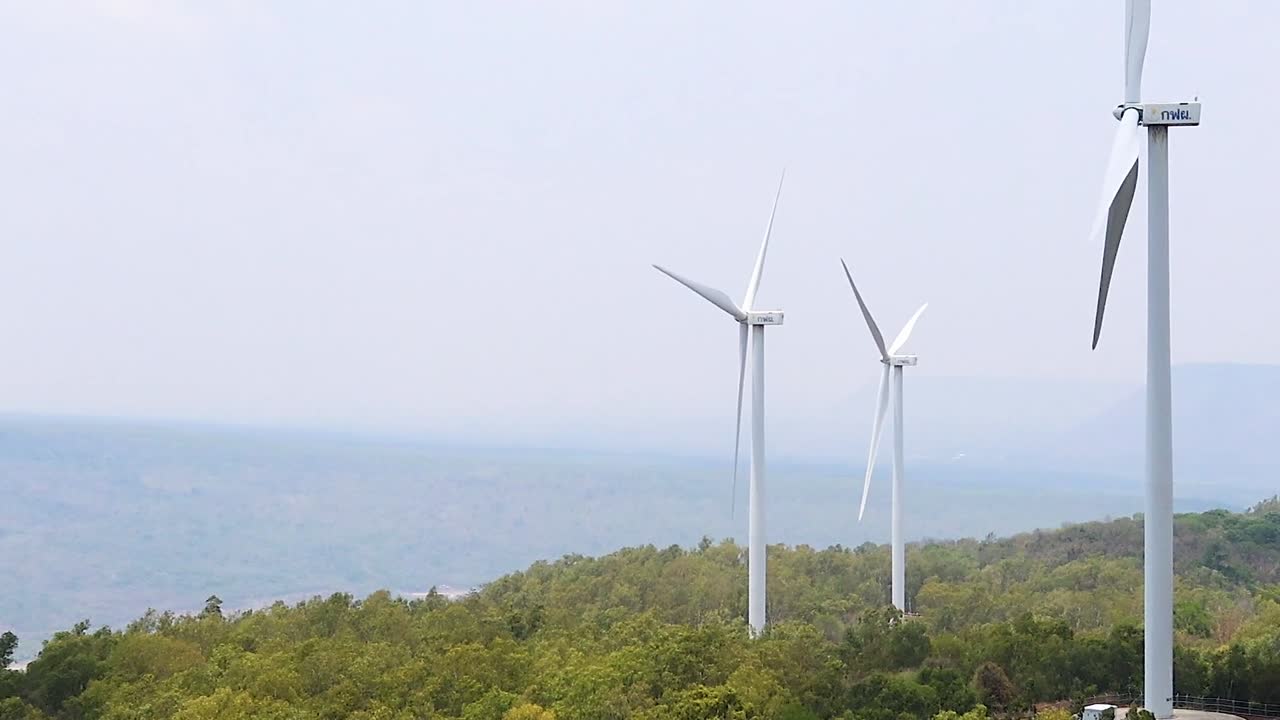 Three wind turbines stand tall over lush green hills with a distant horizon.
