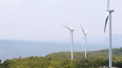 three wind turbines stand tall over lush green hills with a distant horizon.