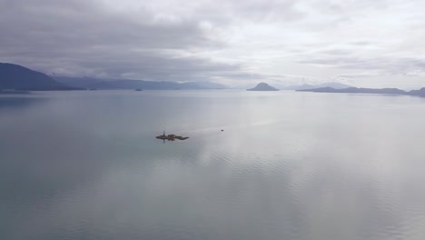 Vista-Aérea-Extremadamente-Amplia-Del-Arrecife-Vanderbilt-Con-El-Barco-De-Buzo-Anclado,-La-Puesta-De-Sol-Y-La-Cordillera-De-Alaska,-Juneau-Ak