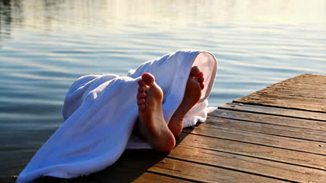 feet wrapped in a white towel relaxing on a wooden dock by the water