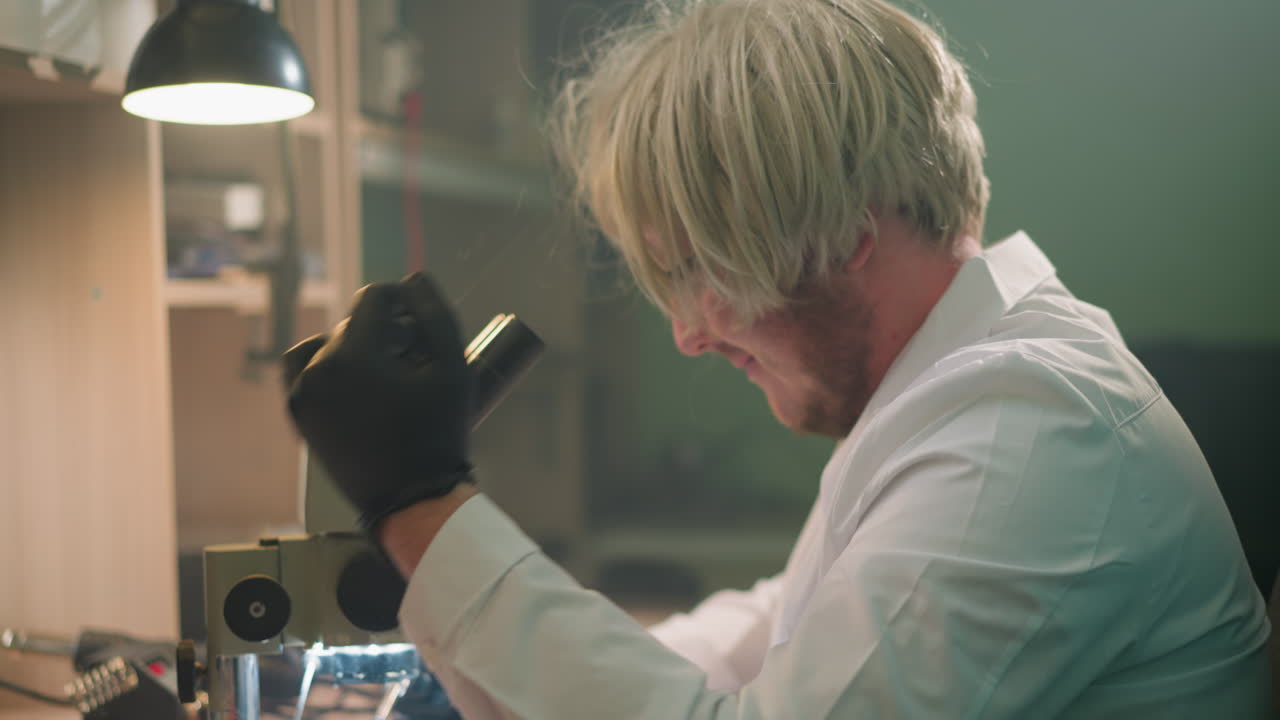 A close-up view of a technician wearing a blonde wig and black gloves, intensely focused on examining a sample under a microscope in a laboratory