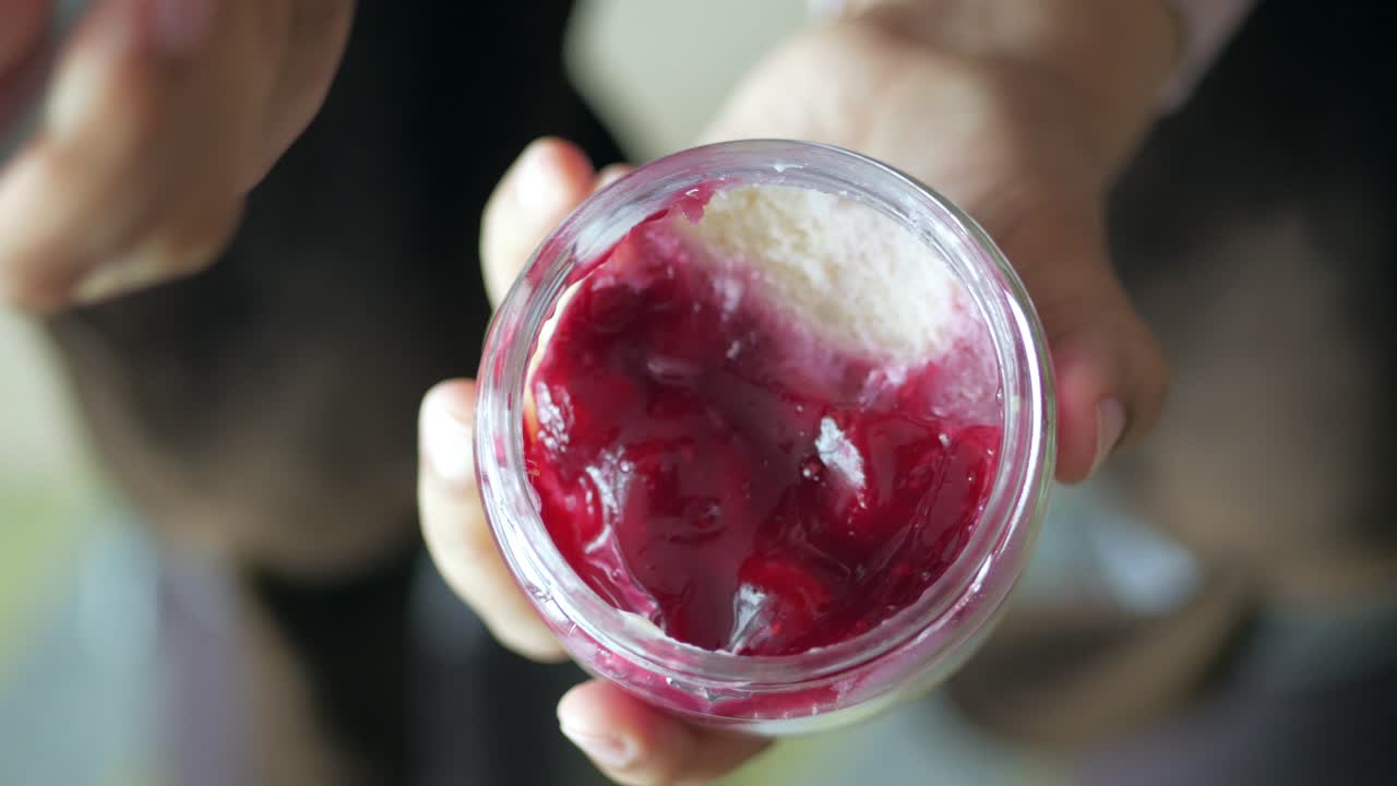 Hand holding a jar of cherry dessert with a spoon