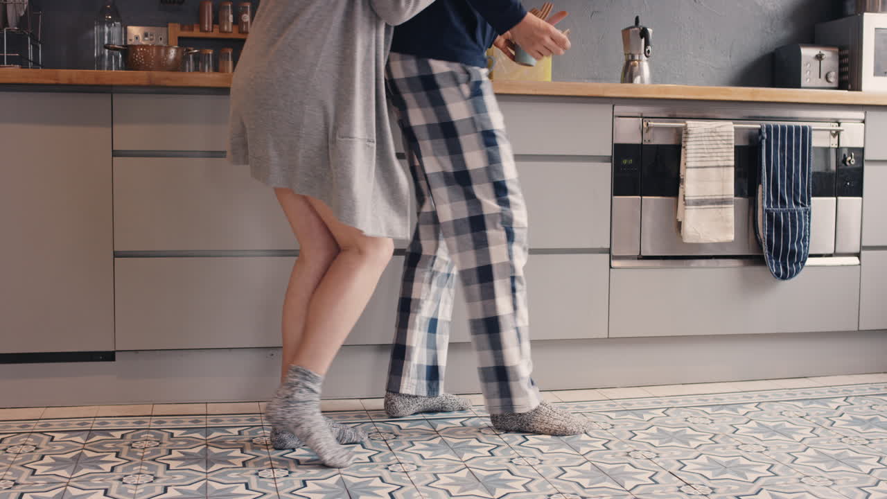 Gladt nygift ungt par danser og lytter til musik i køkkenet iført tøj, om morgenen derhjemme og forelskede