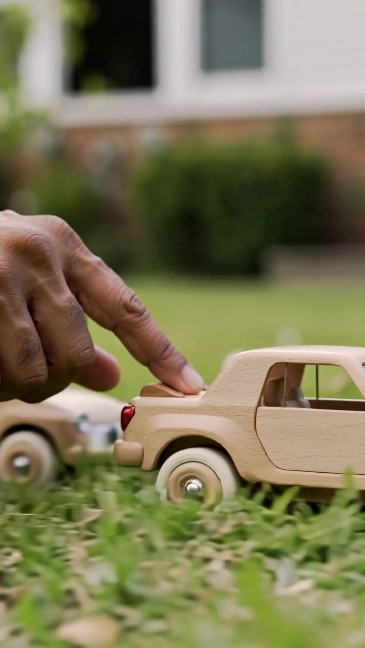 Vertical video: Placing hands nudging two wooden cars on lawn, tapping car to roll away for play