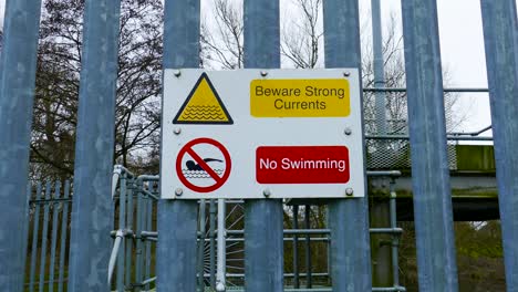 beware strong current and no swimming sign on a barrier metal bar wall