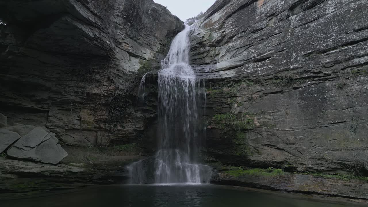 Water flows from la foradada waterfall and creates a small pond surrounded by rocky cliffs and vegetation in les guilleries, catalonia