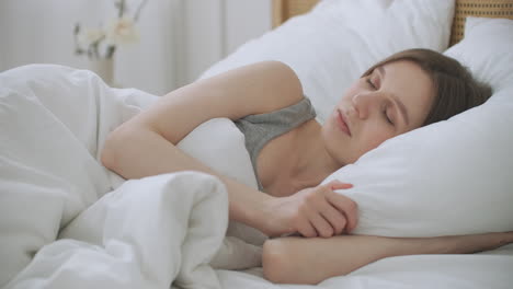 people waking up - young woman opens her eyes on a sunny morning. the girl lies in bed wakes up and sweetly stretches.