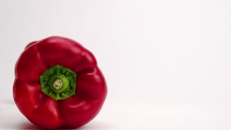 verduras enteras de pimiento rojo brillante que caen sobre la mesa blanca y rebotan entre sí antes de cerrarse en cámara lenta